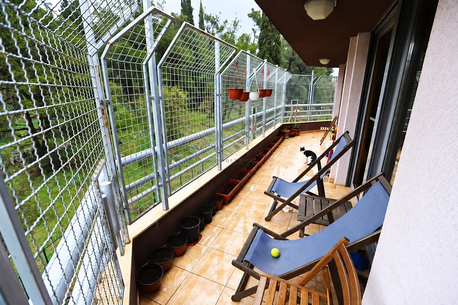 Dugačak prostrani balkon sa stolicama na sklapanje i zaštitnom ogradom.