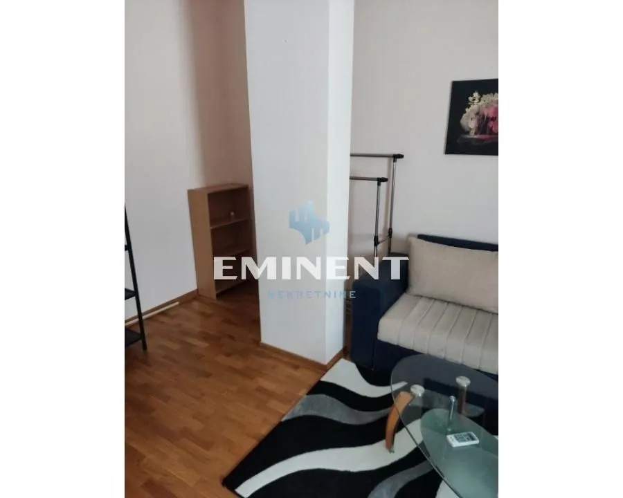 A small section of the living room with a sofa, a glass coffee table, and wooden flooring.