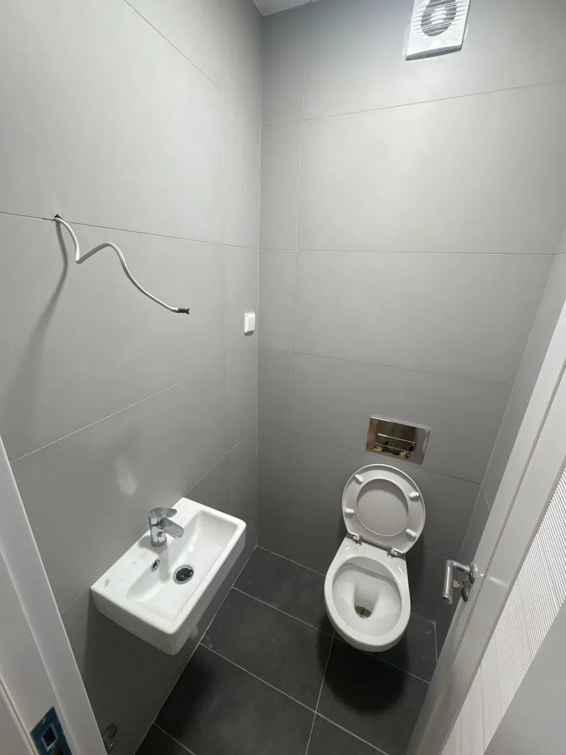 Manje kupatilo sa sijivim pločicama, toaletom i umivaonikom.