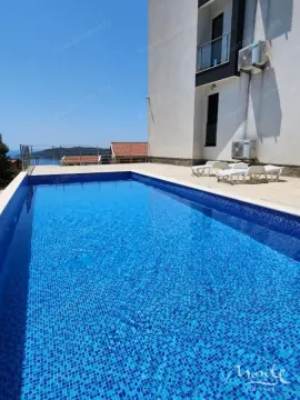 Spoljni bazen sa popločanim platoom ispred stambene zgrade i pogledom na more. - image 13