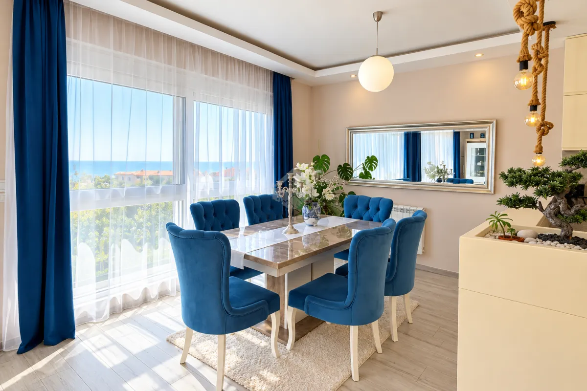 Dining area with a table, blue chairs, and a large window with a sea view.