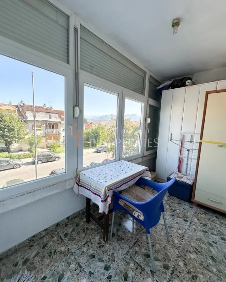 Zastakljeni balkon sa stolom, stolicom i ormarom.