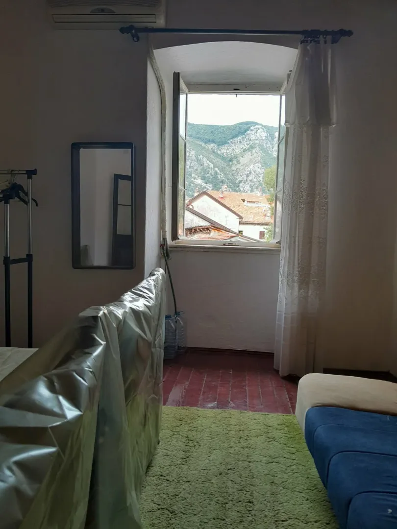 Manja soba sa krevetom prekrivenim zaštitnom folijom i pogledom na planinu kroz prozor.