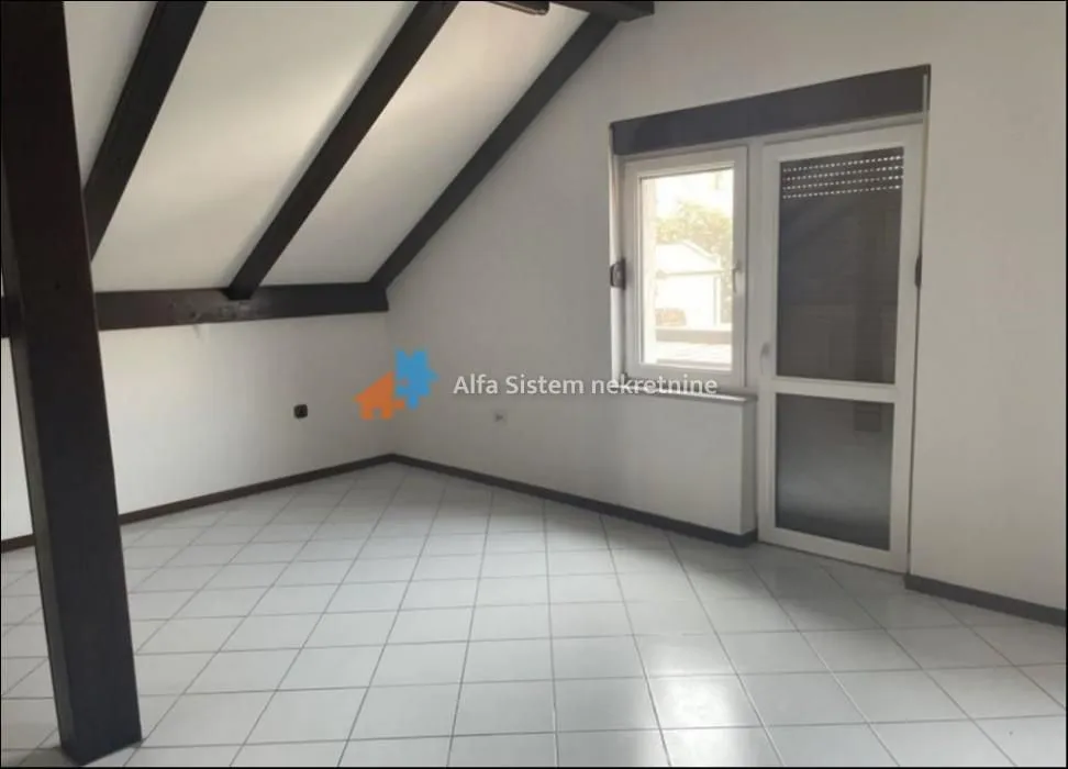Empty attic room with tiled flooring and sloping ceiling with wooden beams.