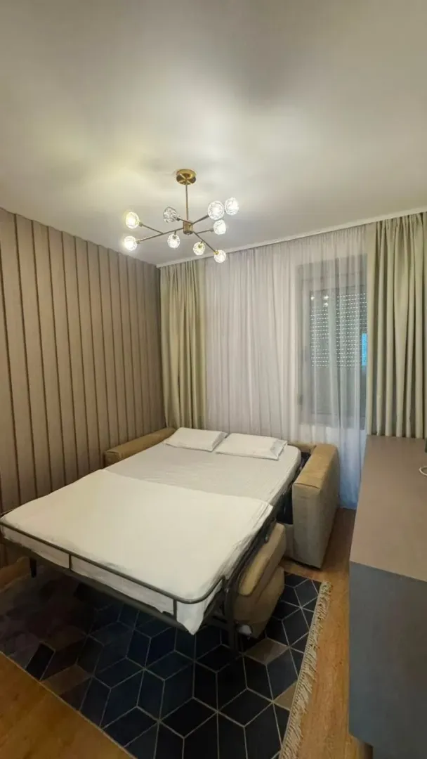 Manja spavaća soba sa rasklopljenim krevetom i ukrasnim lusterom.