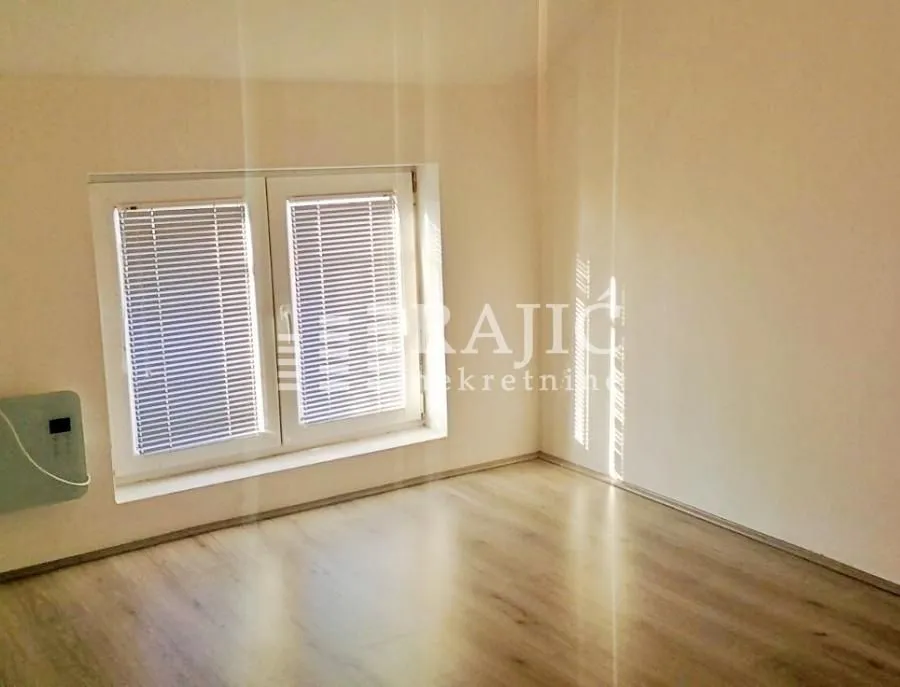 Empty room with laminate flooring and a window with blinds.