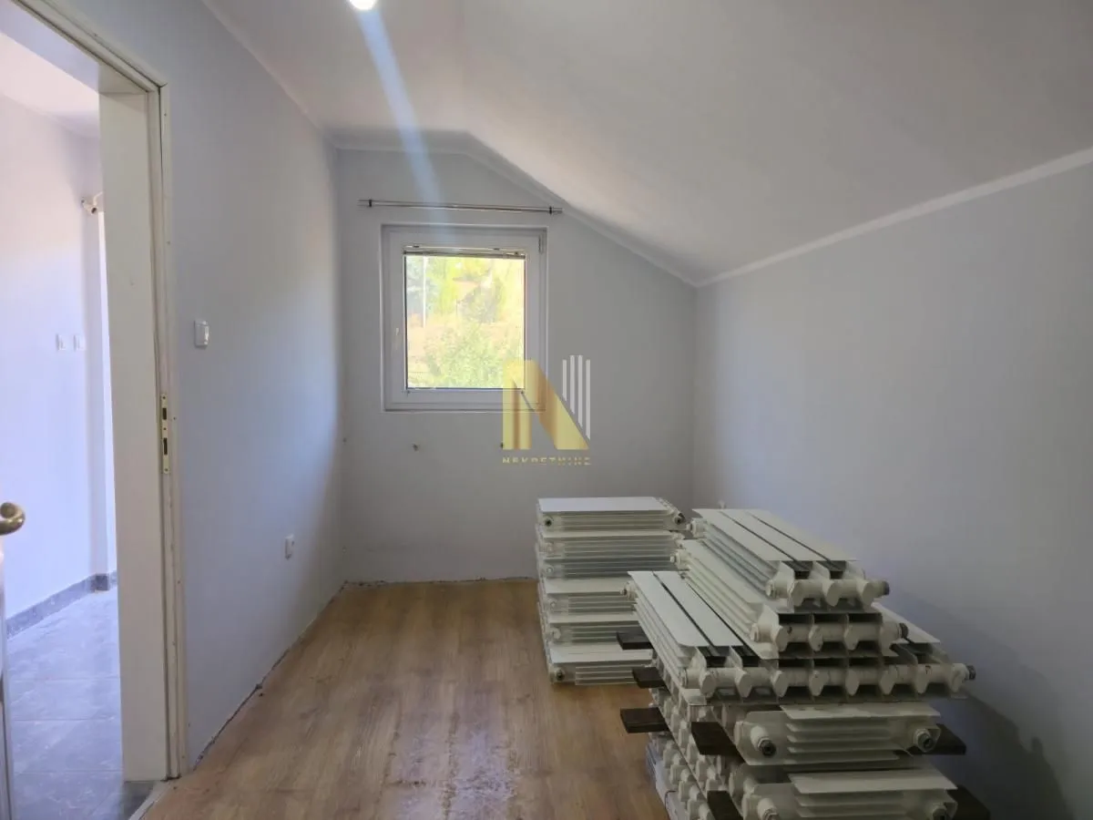 Prazna soba sa kosim plafonom i složenim radijatorima na podu.