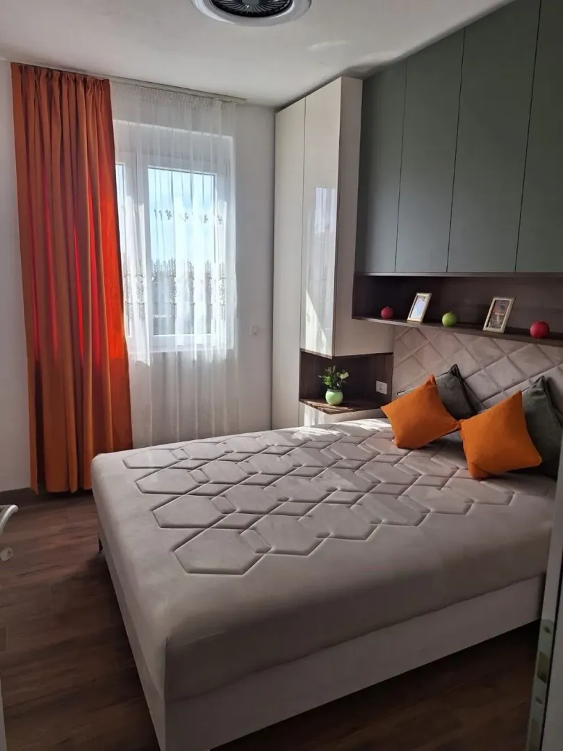 Moderna spavaća soba sa bračnim krevetom, garderoberom i narandžastim detaljima.