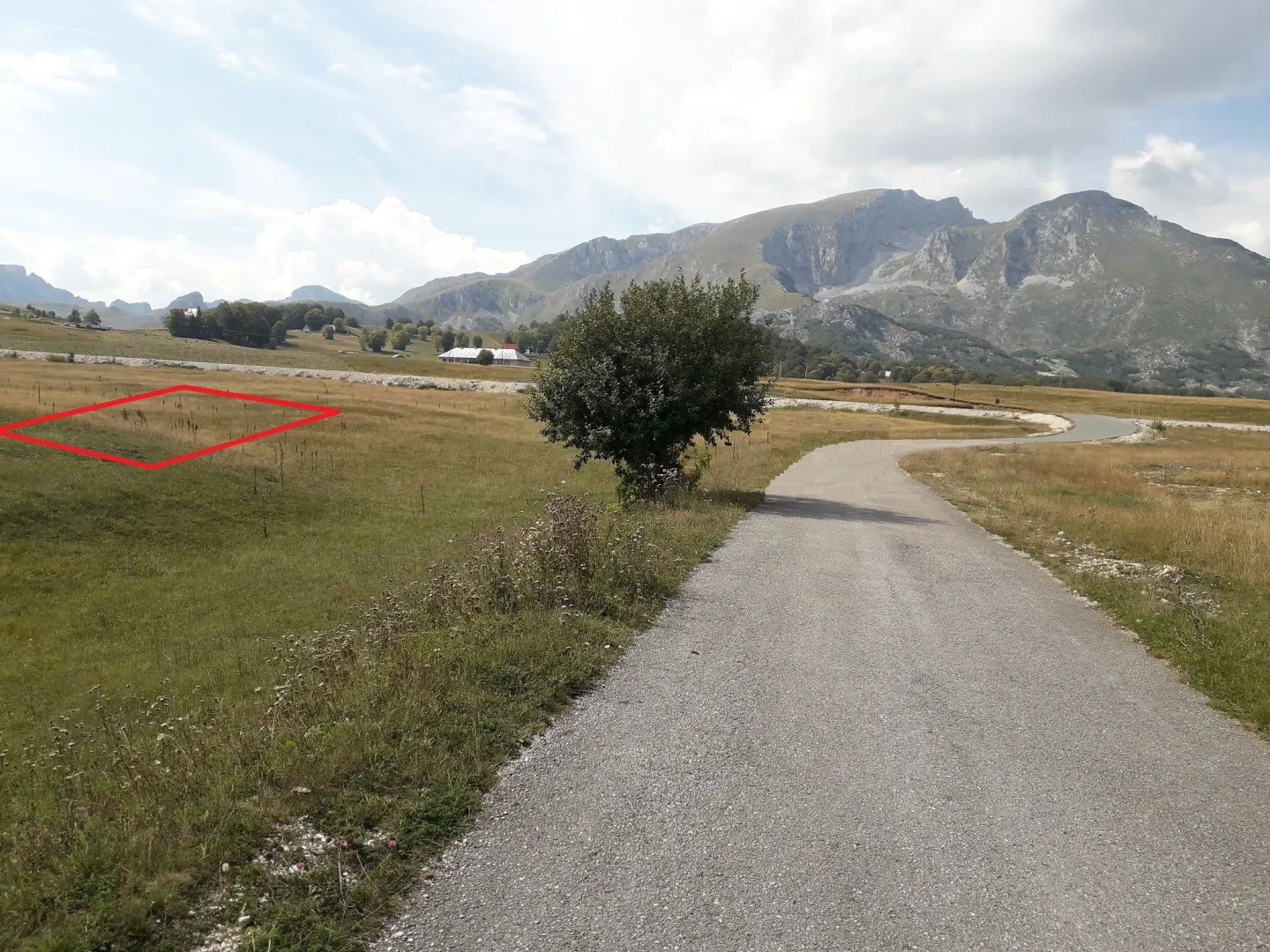 Pogled na plac sa označenom granicom i planinskim pejzažom u pozadini.
