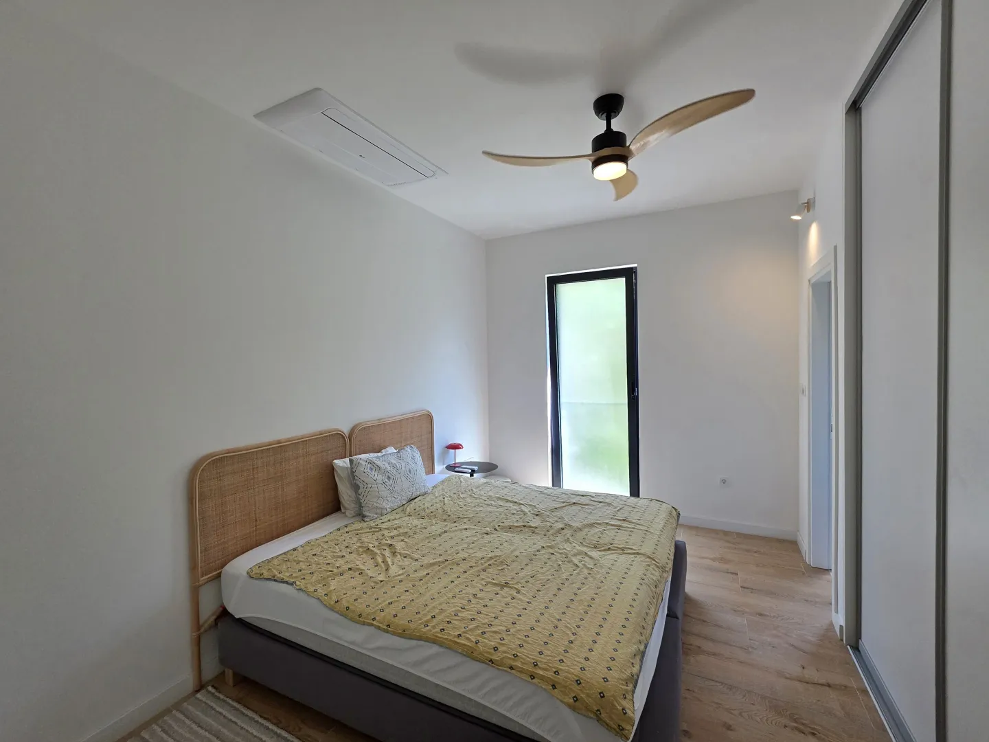 Spavaća soba sa bračnim krevetom, plafonskim ventilatorom i izlazom na terasu.