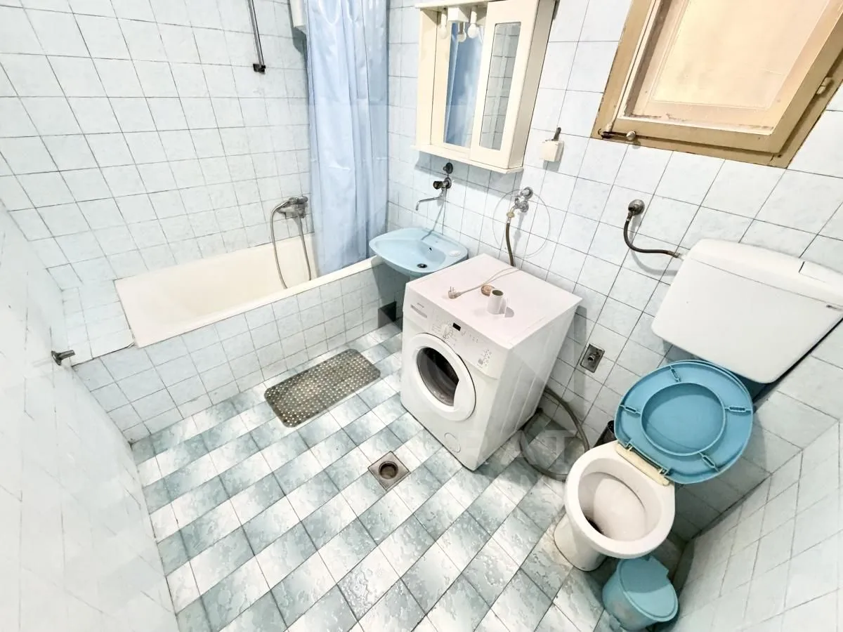 Starije opremljeno kupatilo sa kadom, umivaonikom, veš mašinom i toaletom.