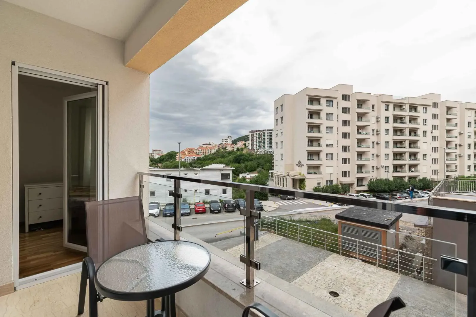 Natkriveni balkon sa stolom i stolicama i pogledom na naselje i okolne zgrade.