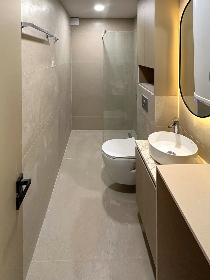 Moderne kupatilo sa tuš kabinom, umivaonikom i WC šoljom u bež tonovima.