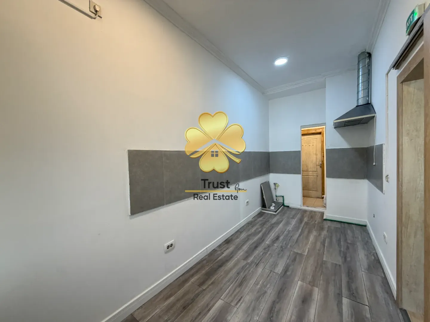 Empty kitchen with grey and white wall tiles and laminate flooring.