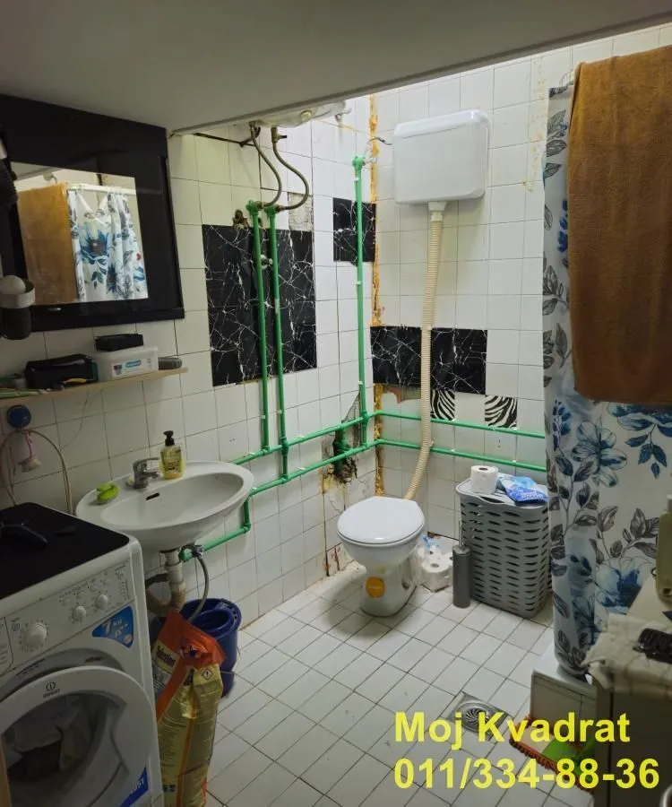 Starije kupatilo sa sanitarijama i vidljivim instalacijama.