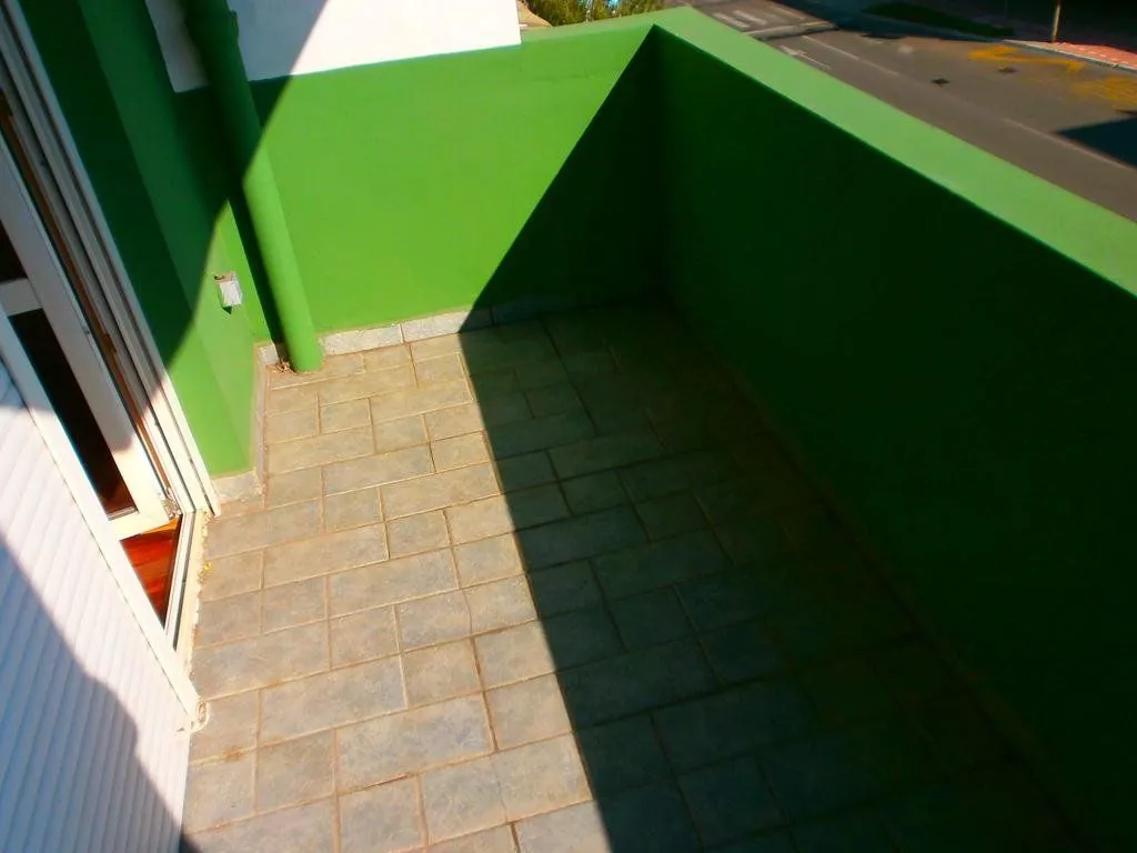 Prazan balkon sa zelenim zidovima i popločanim podom.