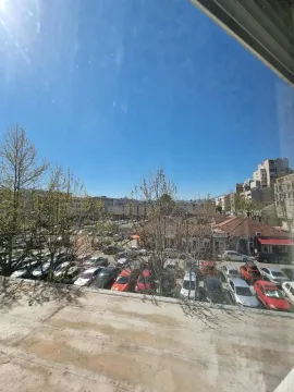 Pogled sa prozora na parking i okolne zgrade pod vedrim nebom. - image 12
