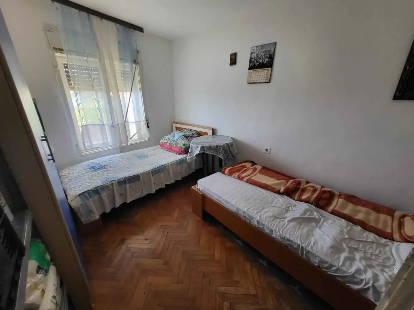 Spavaća soba sa dva kreveta, parketom i prozorom sa zavjesama.
