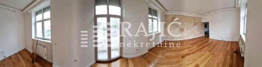 Panoramic view of a spacious living room with wooden flooring and large windows.