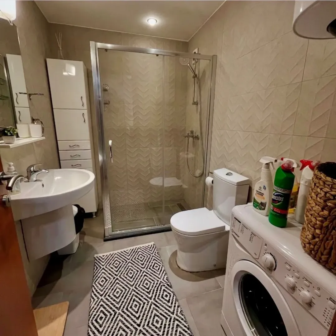 Modern bathroom with a walk-in shower, washbasin, and washing machine.