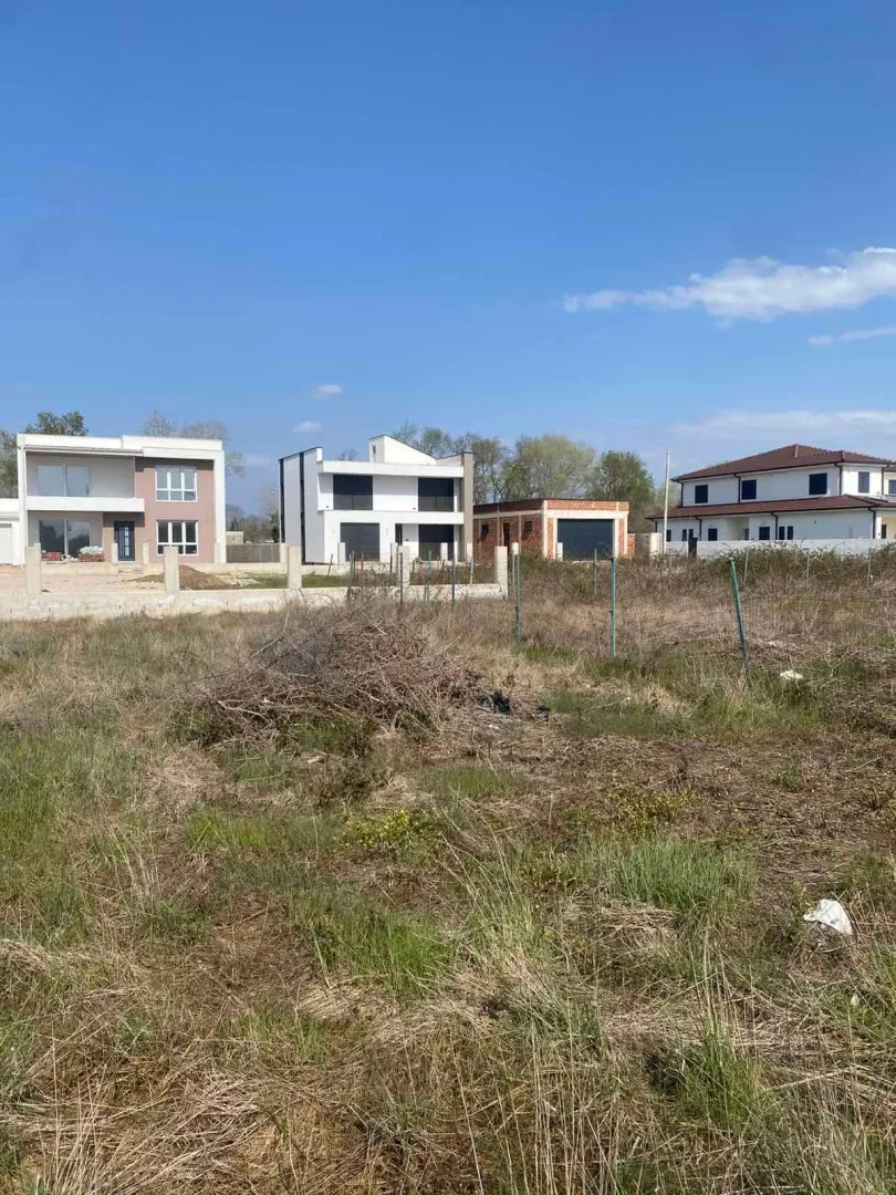 Pogled na plac sa travnatom površinom i okolnim kućama u pozadini.