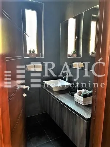 Moderno kupatilo sa tamnim pločicama i umivaonikom na ormariću.