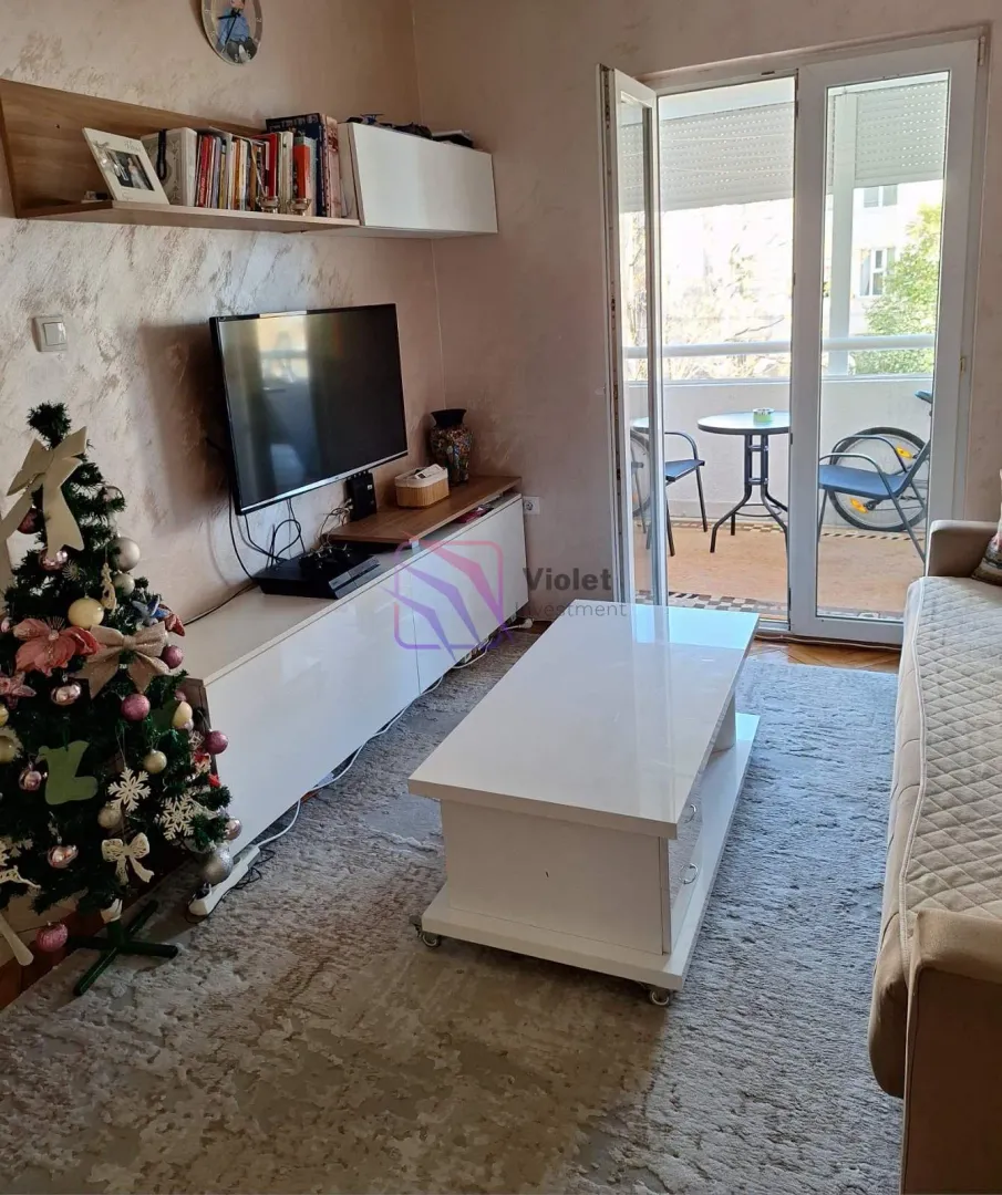 Dnevna soba sa garniturom, TV-om i izlazom na terasu.