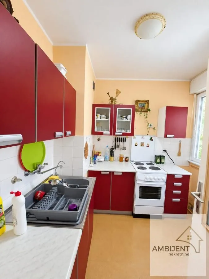 Kuhinja sa crvenim elementima i belom radnom površinom.