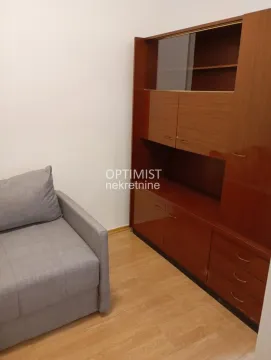 Manja soba sa sivom foteljom na razvlačenje i velikim drvenim ormarom. - image 6