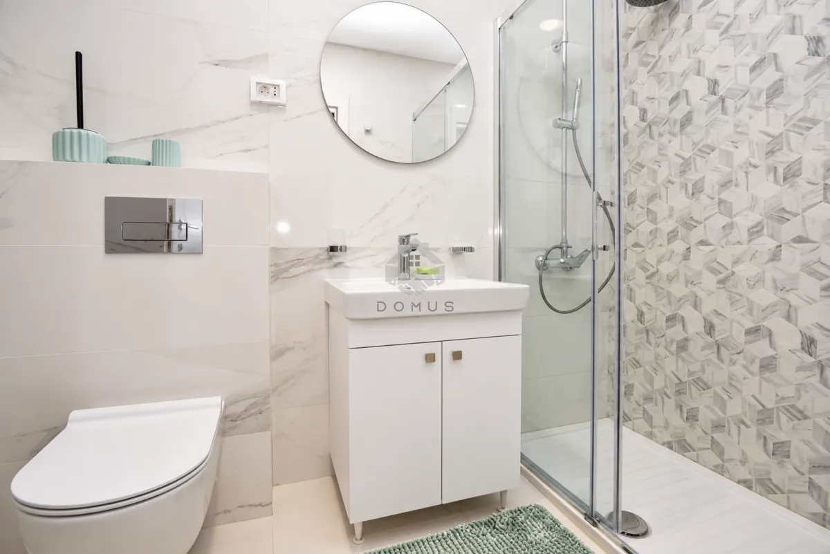 Moderne kupatilo sa tuš kabinom, bijelim umivaonikom i ugradnom šoljom.