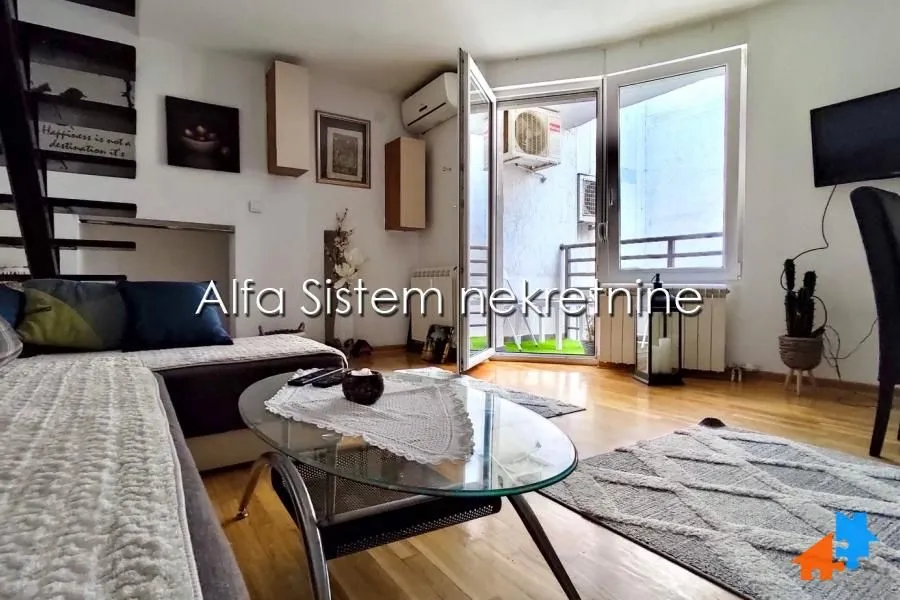 Dnevna soba sa garniturom, staklenim stočićem i izlazom na terasu.