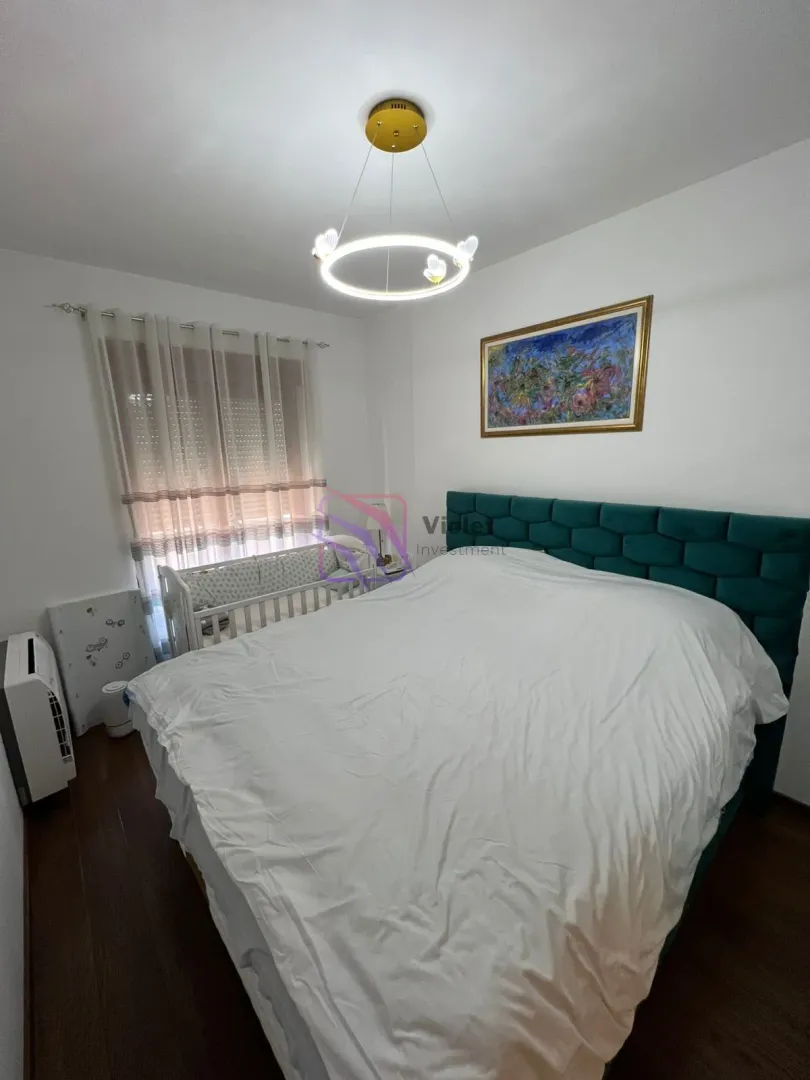 Furnished bedroom with a double bed, baby crib, and a modern chandelier.