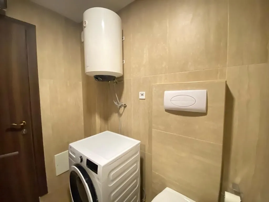 Small bathroom clad in ceramic tiles with a concealed toilet, washing machine, and water heater.