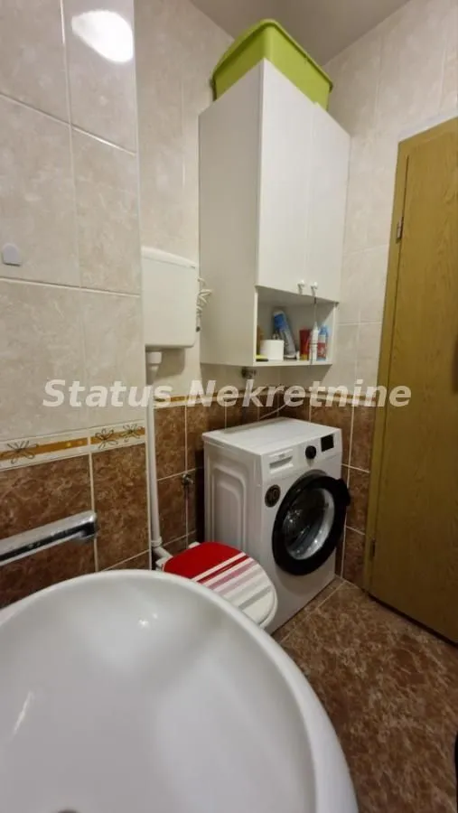 Kupatilo sa umivaonikom, veš mašinom i zidnim ormarićem.