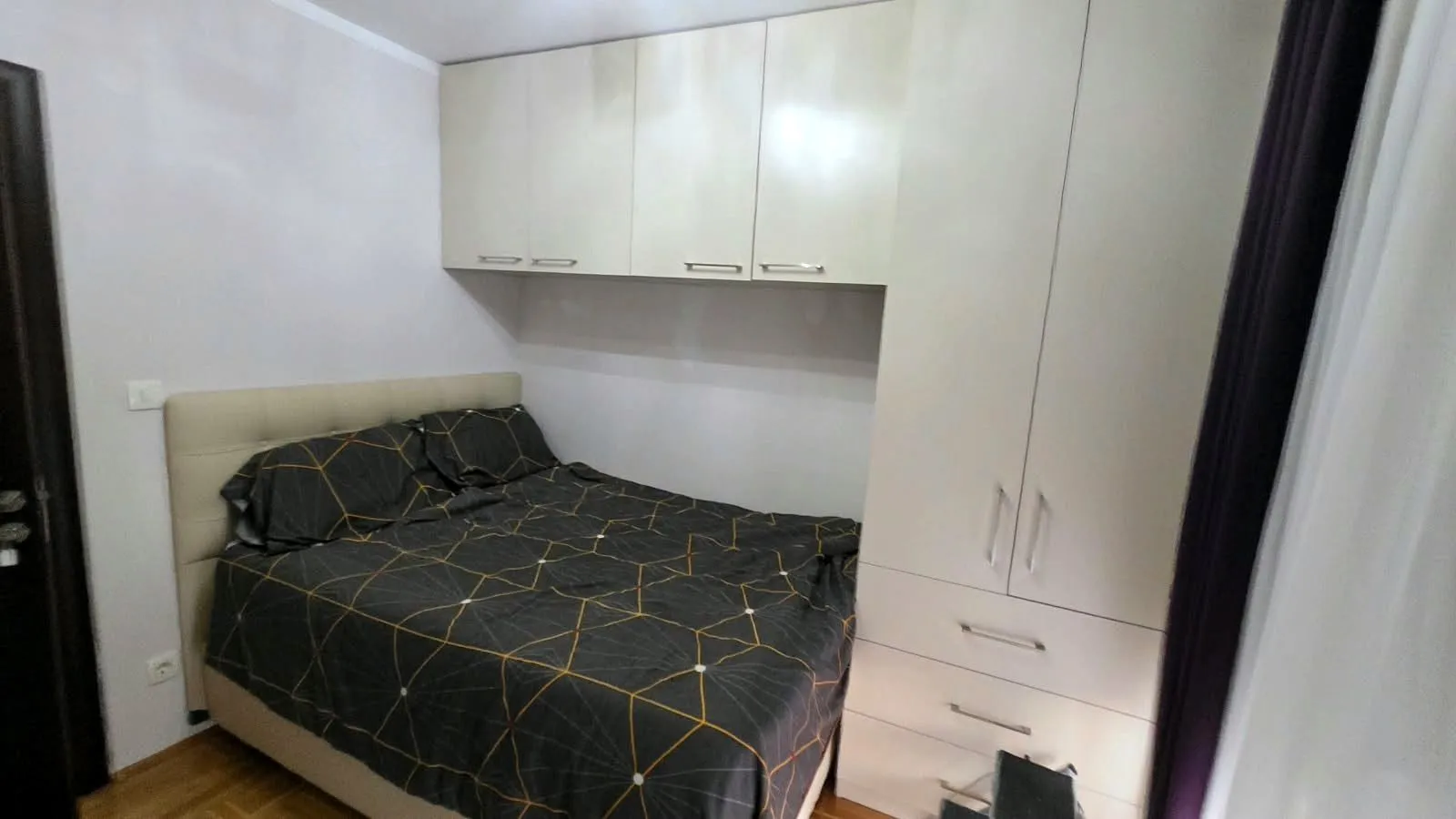 Namještena spavaća soba sa bračnim krevetom, garderoberom i visećim elementima.