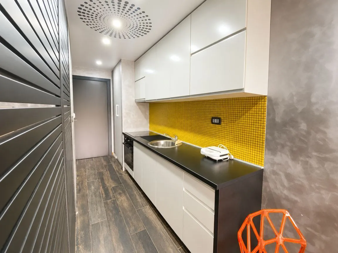 Small kitchen with white cabinets and a yellow mosaic backsplash.