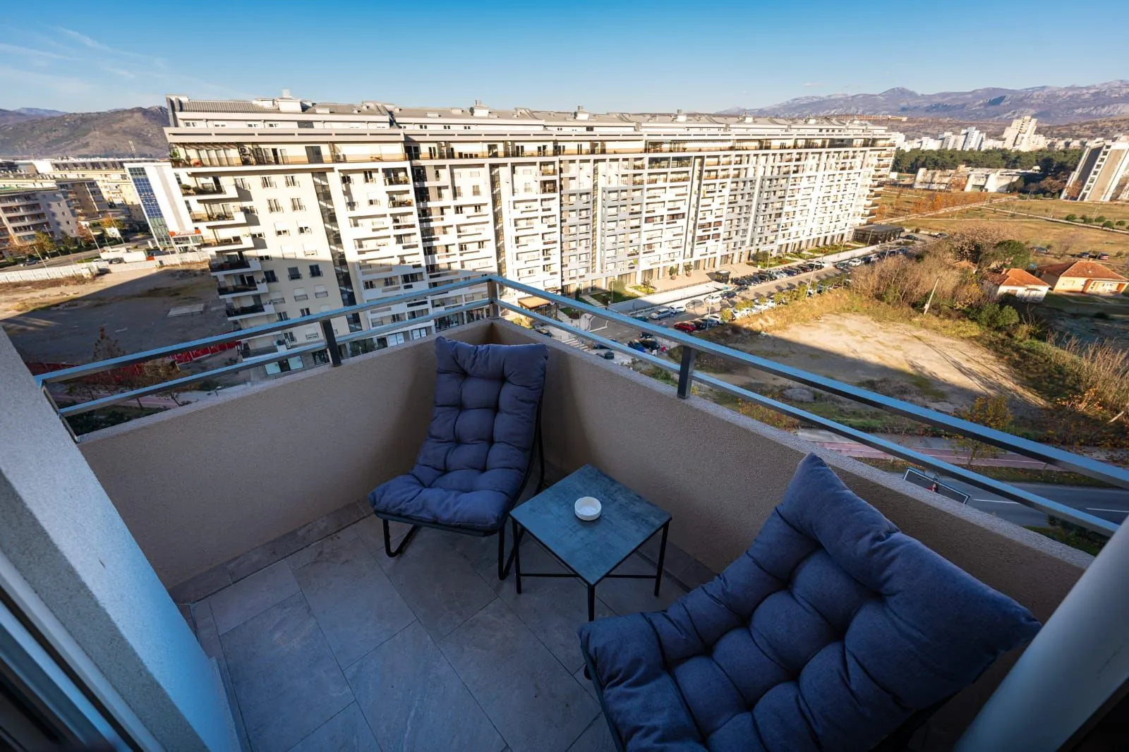 Small furnished balcony with two armchairs and a small table, overlooking buildings and surroundings.