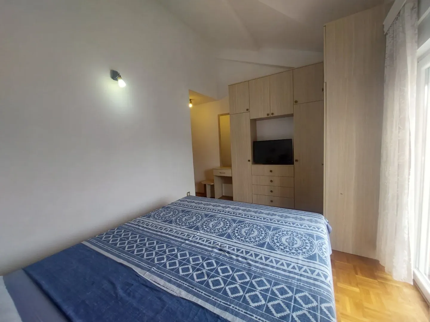 Namještena spavaća soba sa bračnim krevetom, plakarom i televizorom.