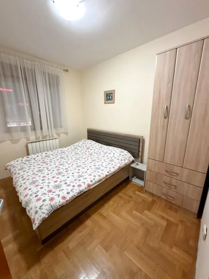 Spavaća soba sa bračnim krevetom, drvenim parketom i ormarom.