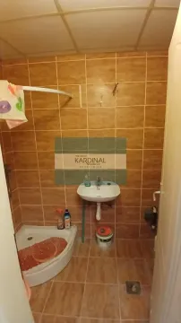 Manje kupatilo obloženo smeđim pločicama sa tuš kabinom i umivaonikom. - image 8