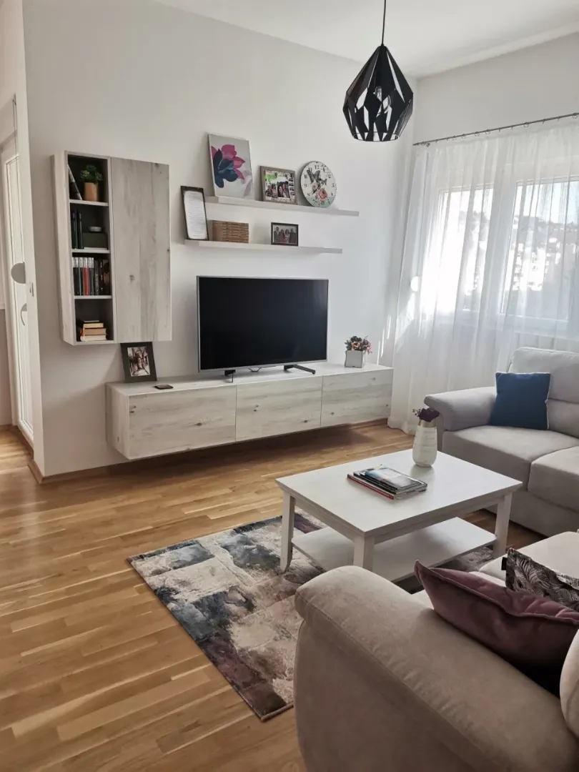 Svijetla dnevna soba sa TV policom i garniturom.