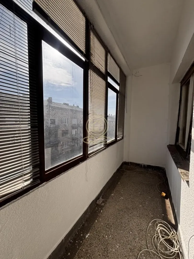 Zastakljeni balkon sa roletnama i pogledom na susedne zgrade.