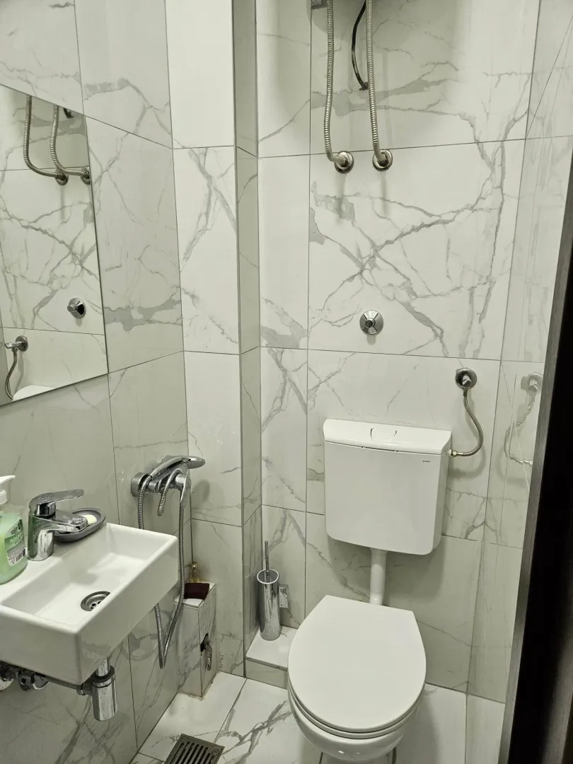 Smaller bathroom tiled with marble-pattern tiles, featuring a toilet and a washbasin.