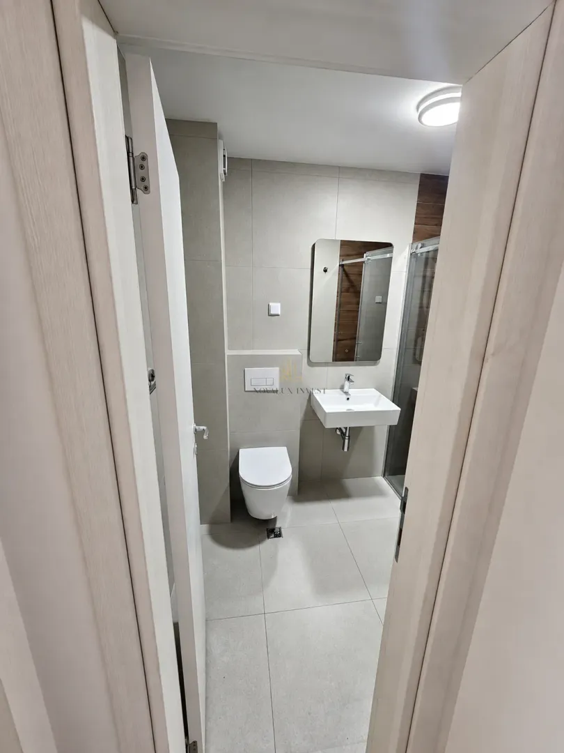 Pogled iz hodnika na moderno uređeno kupatilo sa sanitarijama i tuš kabinom.