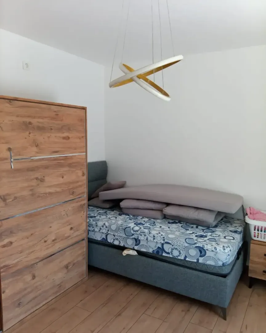 Small bedroom with a bed, wooden wardrobe, and a modern chandelier.
