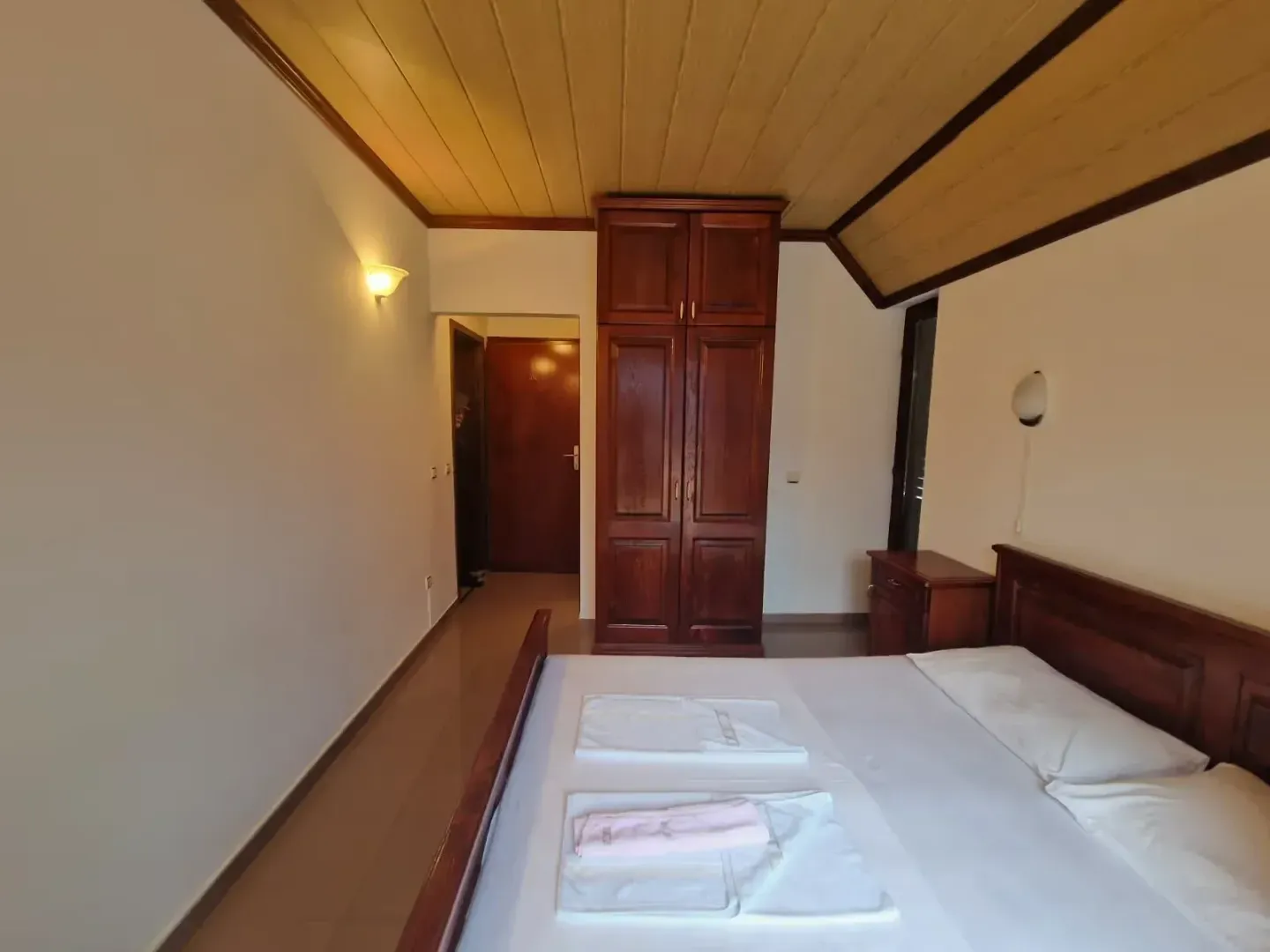 Bedroom with a double bed, wooden wardrobe, and wood-paneled ceiling.