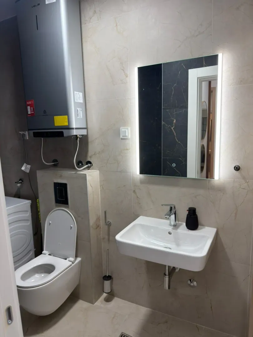 Moderne kupatilo sa umivaonikom, WC šoljom, ogledalom i bojlerom.