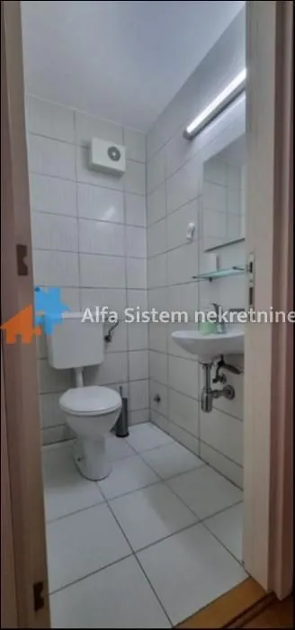 Manje kupatilo obloženo svetlim pločicama sa toaletom i umivaonikom.