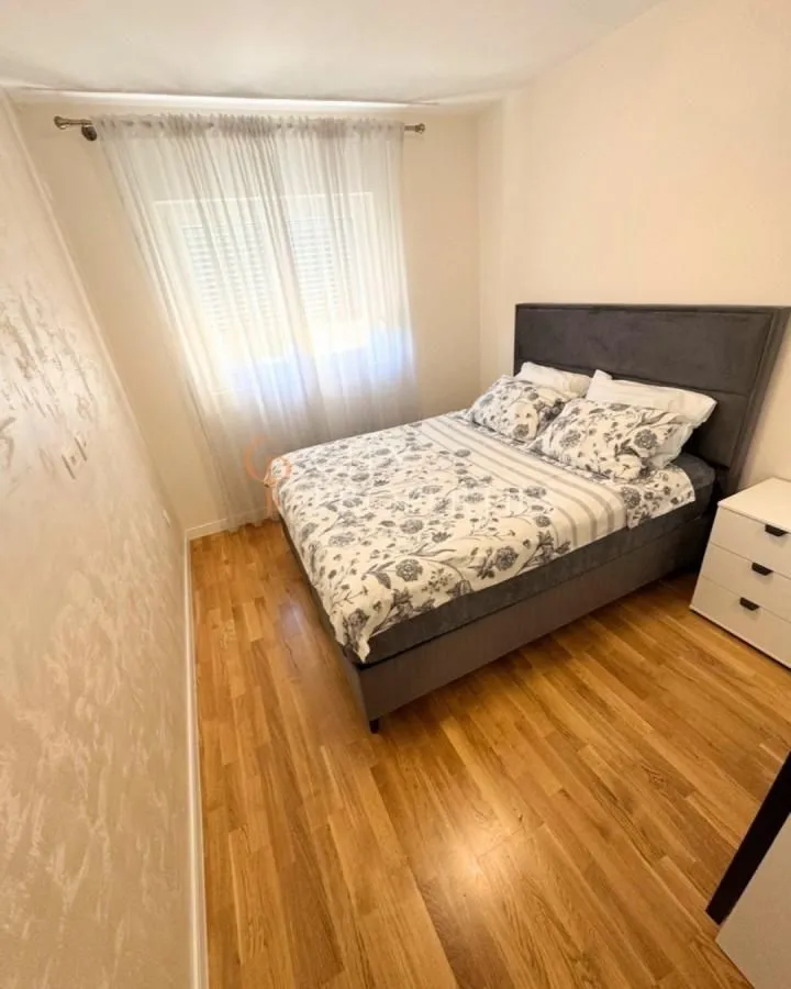 Furnished bedroom with a double bed, white nightstand, and a window with curtains.