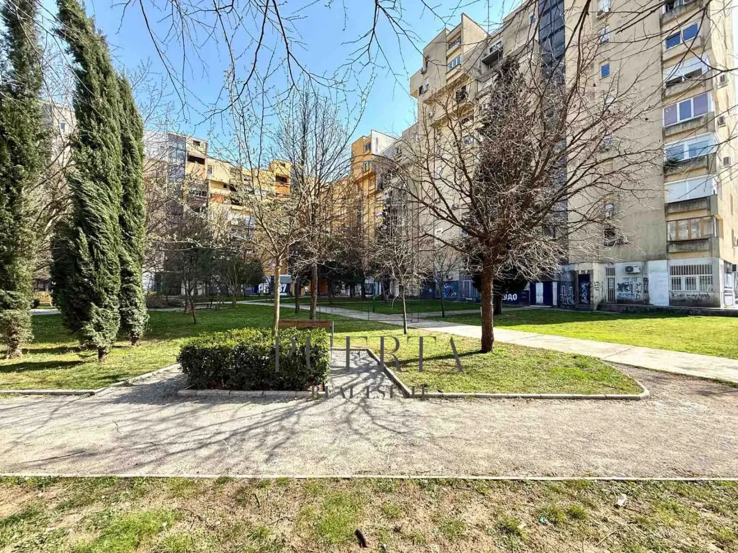 Zelena površina i drveće ispred stambene zgrade.